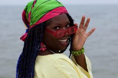 Josie is wearing an 80's colour-blocked scarf around her head, 80's yellow cotton cover up, 90's inspired sun glasses, wood bangles and earrings  from the shop.