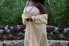 Josie is wearing a monochromatic custom-made polyester maxi dress and woven cover up as a set, with wood accessories all from the shop.