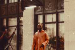 Tahir, wearing 90's red vinyl rain coat, 80's Adidas high-top sneakers.